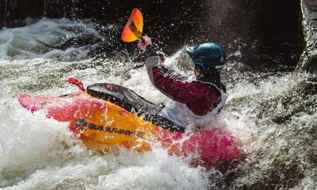 Kajakarz w kajaku jedynce walczy z rwącym nurtem, rozpryskując wodę.