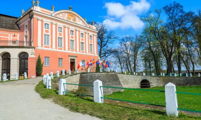 Pałac w Kurozwękach, z flagami narodowymi przed wejściem, zaprasza do odkrywania jego atrakcji.