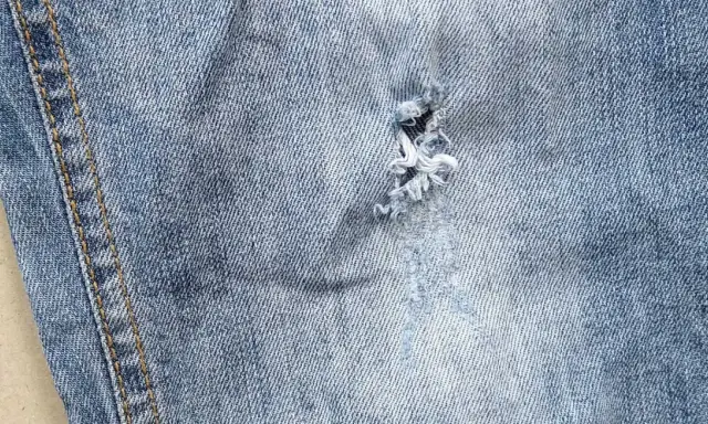 Jak zaszyć dziurę w spodniach dresowych? Widok z bliska na przetarty jeans z widocznym uszkodzeniem, które można naprawić.