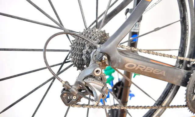 Tylna przerzutka Shimano Ultegra, kluczowy element przekładni rowerowej, na tle koła i ramy Orbea.