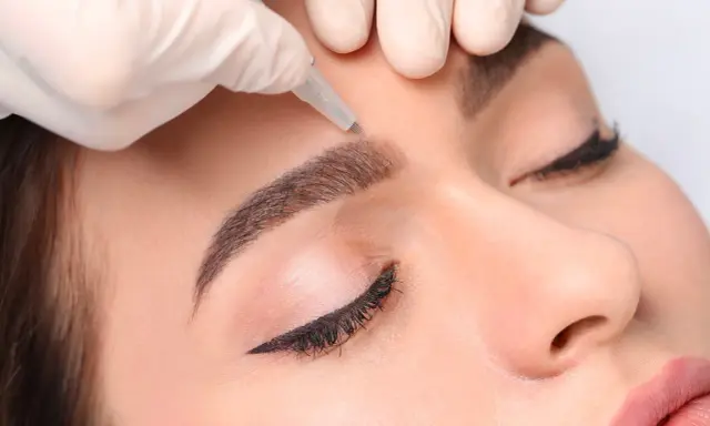 Main d'une esthéticienne réalisant des sourcils permanent effet naturel sur une cliente.