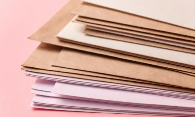 Stos papierów w różnych odcieniach brązu i różu. Różne rodzaje papieru, od kraftowego po delikatnie barwiony, tworzą ciekawą kompozycję.