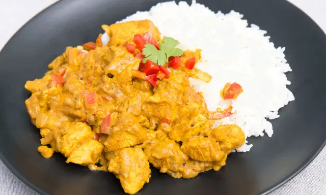 Pyszny kurczak curry z ryżem, udekorowany papryką i natką kolendry, podany na czarnym talerzu.