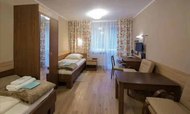 Pokój w sanatorium Włókniarz Busko-Zdrój: dwa łóżka, szafa, biurko z komputerem i stolik.