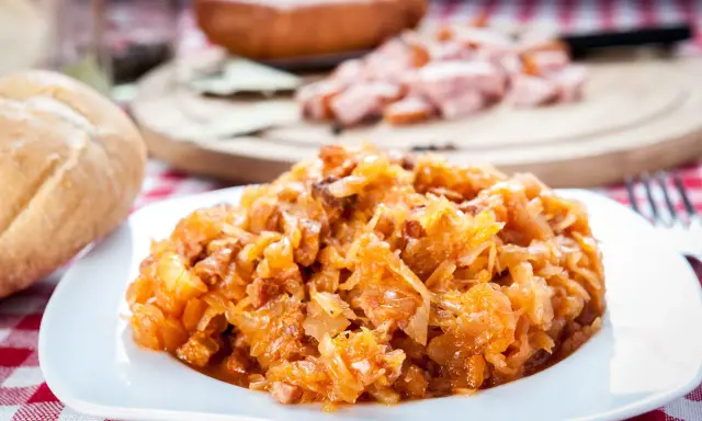 Pyszny bigos Ani, gotowany z pasją, na talerzu. Obok bułka i kawałki kiełbasy.
