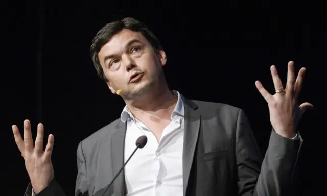 Economist Thomas Piketty spreekt met gebaren, zijn handen omhoog, terwijl hij een lezing geeft.