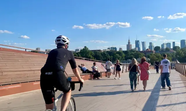 Rowerzysta na moście w Warszawie, w tle panorama miasta. Idealne miejsce na odkrywanie tras rowerowych Warszawa i okolice.
