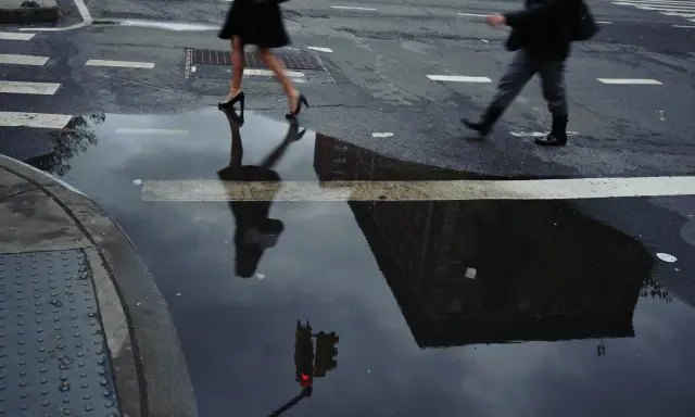 Jay Maisel photography captures a rainy street scene with blurred figures crossing, their reflections distorted in puddles, mirroring the city's mood.
