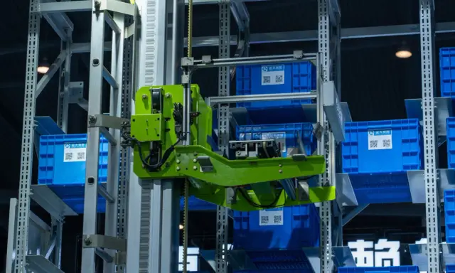 Automatyczny magazyn z niebieskimi pojemnikami. Zielony mechanizm pobiera jeden z nich. To przykład, co to jest telemetria w działaniu.