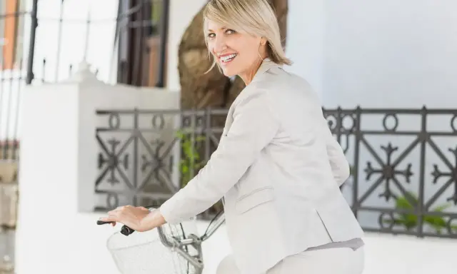 Donna sorridente in bicicletta, con un elegante outfit che valorizza la sua figura. Un look chic per una donna di 45 anni.