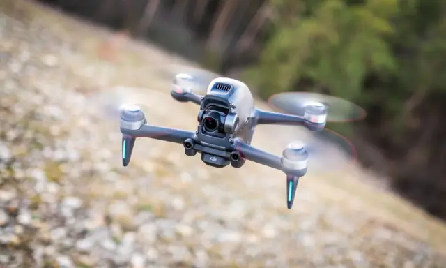 Eine FPV Drohne fliegt über steinigen Boden. Sie hat eine Kamera vorne und leuchtende blaue Lichter an den Armen.