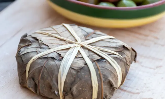 Un mets emballé dans des feuilles séchées, lié par des brins, évoquant les spécialités des Hautes-Alpes.