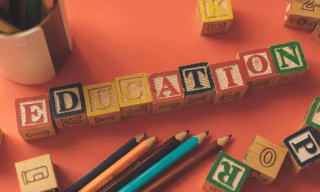 Klocki z literami tworzą napis EDUCATION. Obok leżą kredki i inne klocki, idealne do nauki tekstów po angielsku B2.