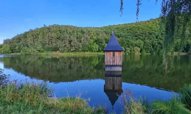 Holzhaus mit spitzem Dach, wie eine kleine Kirche im See, spiegelt sich im ruhigen Wasser.