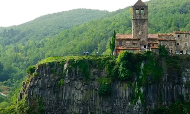 Castillo medieval en un acantilado, uno de los pueblos de Girona, rodeado de vegetación exuberante.