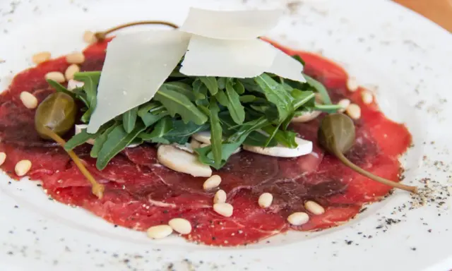 Delicato carpaccio di manzo con rucola, scaglie di parmigiano, pinoli, capperi e funghi champignon.