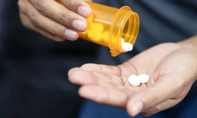 Dłoń wysypuje białe tabletki z pomarańczowego pojemnika. Czy to oxycodone? Co to jest i jak działa?