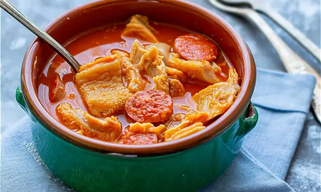 Un cuenco verde con callos a la madrileña, trozos de chorizo y un tenedor.