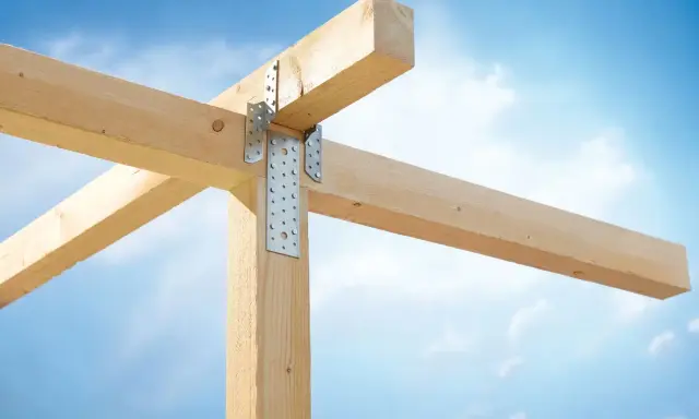 Stabile Holzverbindungen mit Metallwinkeln sichern die Balkenkonstruktion gegen den blauen Himmel.