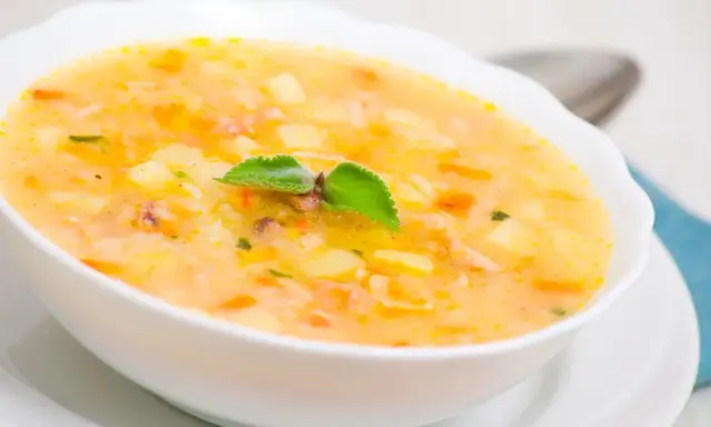 Una ciotola di zuppa cremosa con pezzi di patate e riso, guarnita con una foglia verde. Un piatto confortante che sa di casa.
