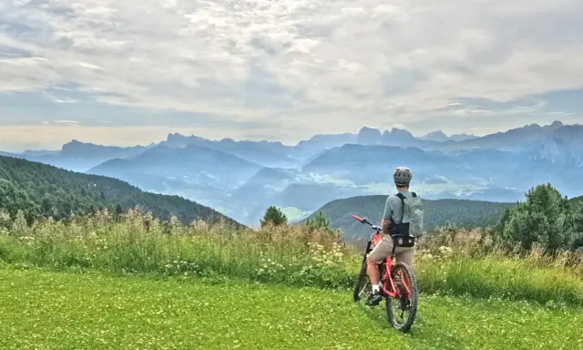 Ciclista con bici da enduro ammira il panorama montano. Un'avventura in bici, forse a Cervia, tra prati fioriti e cime nebbiose.