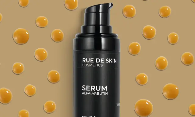 Serum z alfa-arbutyną od RUE DE SKIN. Krople serum unoszą się na beżowym tle, tworząc efekt kropli rosy.