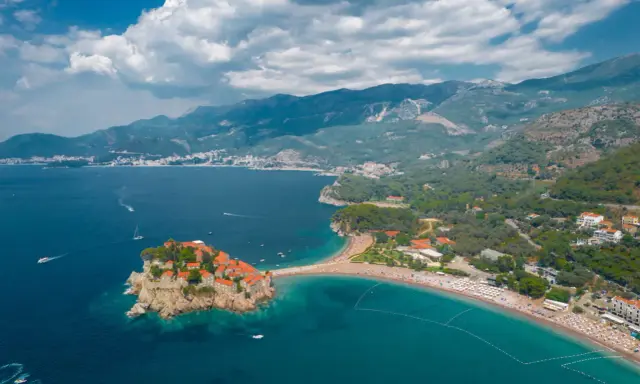 Malownicza wyspa Sveti Stefan, połączona z lądem piaszczystą mierzeją, otoczona turkusowym morzem i górami.