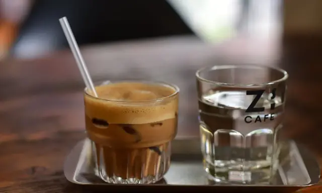 Kawa z lodem i słomką obok szklanki wody. Czy kawa jest moczopędna? Z's Cafe.