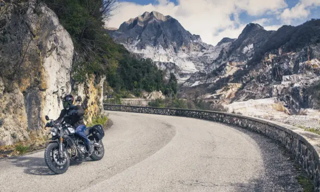 Motociclista su strada tortuosa con montagne di marmo sullo sfondo, un'autentica **Toscana da visitare**.