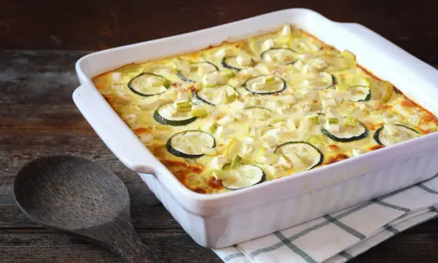 Un gratin de courgettes à l'ancienne, doré et crémeux, garni de rondelles de courgettes et de poireaux, prêt à être dégusté.
