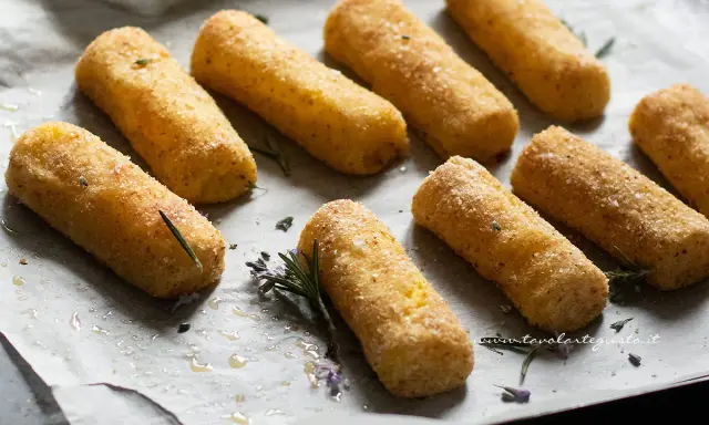Crocchette di patate al forno dorate e croccanti, adagiate su carta forno con rametti di rosmarino e fiori di lavanda.