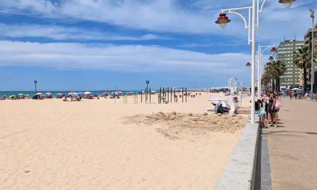 Sonniger Tag am Playa Victoria in Cádiz. Menschen entspannen sich unter bunten Sonnenschirmen, während Kinder am Strand spielen.