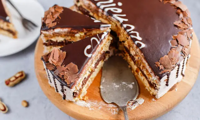 Pyszny tort snickers bez pieczenia, udekorowany czekoladą i wiórkami. Idealny na deser!