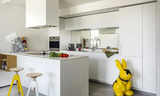 Cucina moderna con isola centrale e sgabelli. La differenza tra RAL 9003 e 9010 è sottile, ma qui il bianco puro domina, con un tocco di giallo dato da un coniglio decorativo.