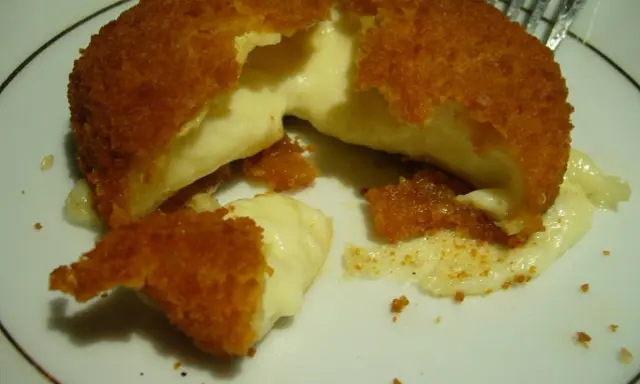 Złocisty camembert w panierce z rozpływającym się, kremowym wnętrzem na białym talerzu.