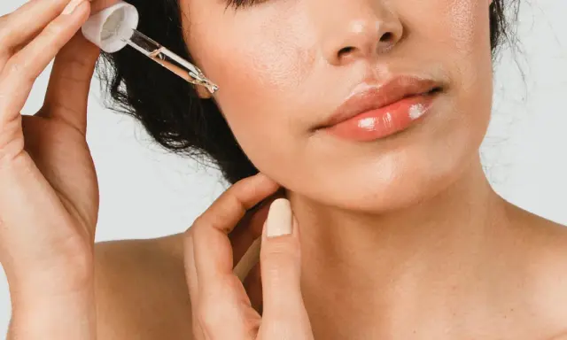 Une main applique une goutte d'huile de ricin visage sur la peau. Les lèvres sont brillantes, la peau est lumineuse.