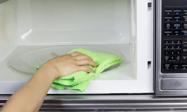 Mano con paño verde limpiando el interior de un microondas.