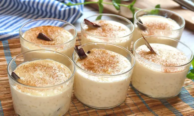 Seis vasitos de arroz con leche cremoso, espolvoreados con canela y decorados con una rama de canela. ¡Perfecto para aprender como hacer arroz con leche!