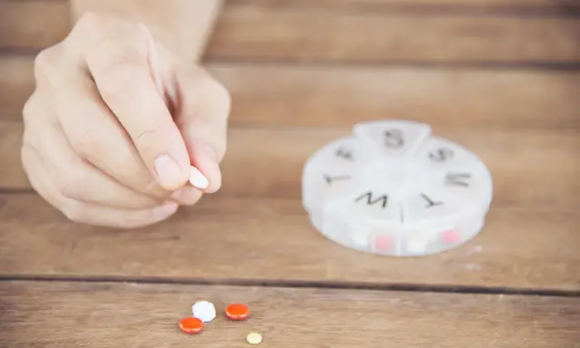Dłoń trzyma tabletkę. Obok leżą inne pigułki i pojemnik na leki. Captopril 12,5 mg jak długo działa?