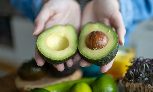 Hände halten eine aufgeschnittene Avocado. Tipps für avocado haltbar machen.