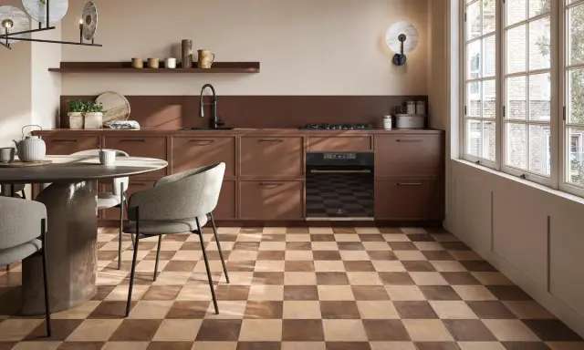 Cucina moderna con pavimento a scacchiera che crea una **tabella colori caldi**. Mobili marroni, tavolo rotondo e sedie grigie.