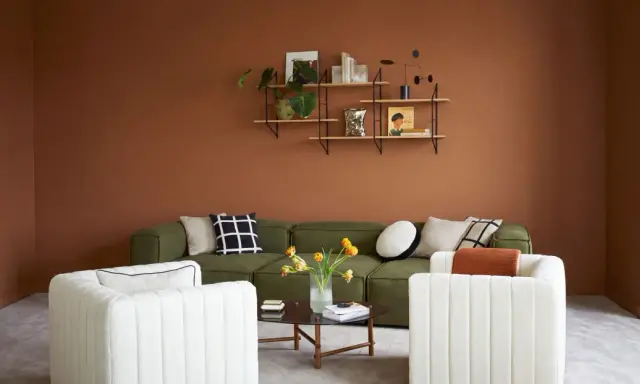 Salon cosy aux murs couleur cognac, canapé vert, fauteuils blancs et table basse.