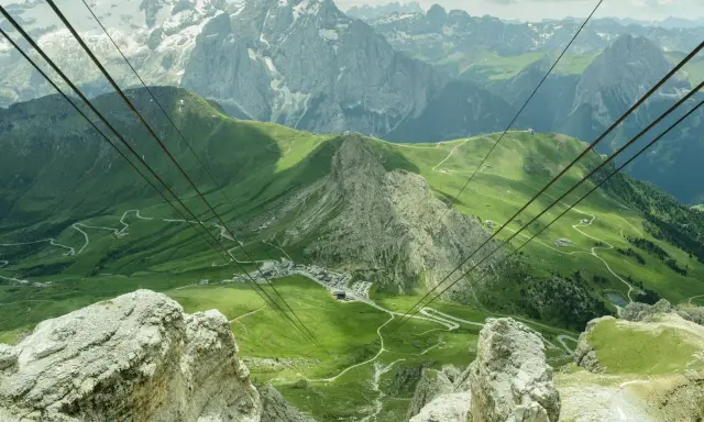 Vista mozzafiato dal passo Pordoi, con montagne innevate, verdi pendii e una strada tortuosa.