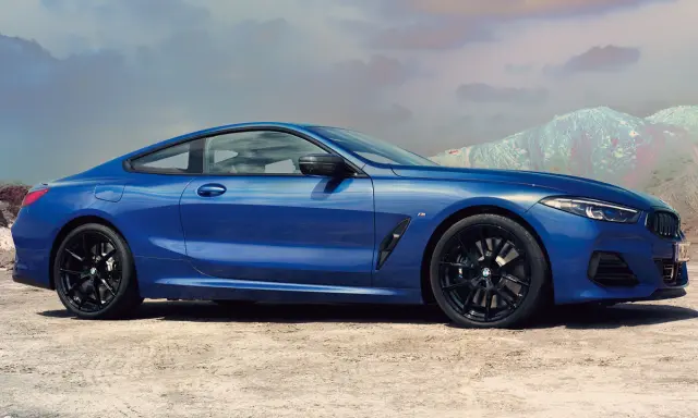 Błękitne BMW 840i z czarnymi felgami na tle pustynnego krajobrazu i gór.