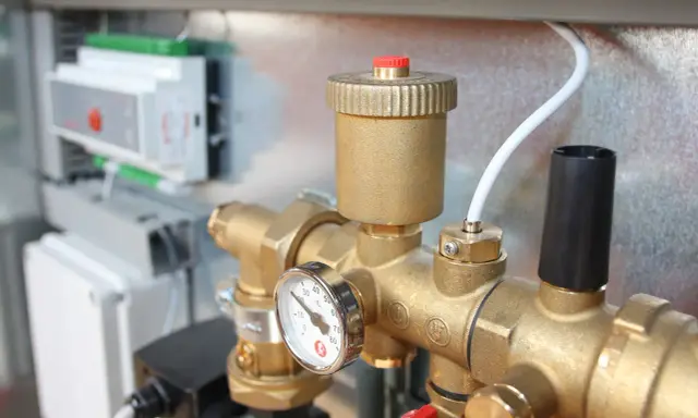 Detalle de tuberías de latón con manómetro y una válvula de seguridad. En el fondo, un panel de control.