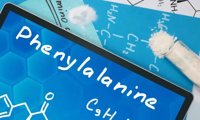 Na ekranie tabletu nazwa "Phenylalanine" i wzór chemiczny. Obok proszek fenyloalaniny w probówce i na kartce.