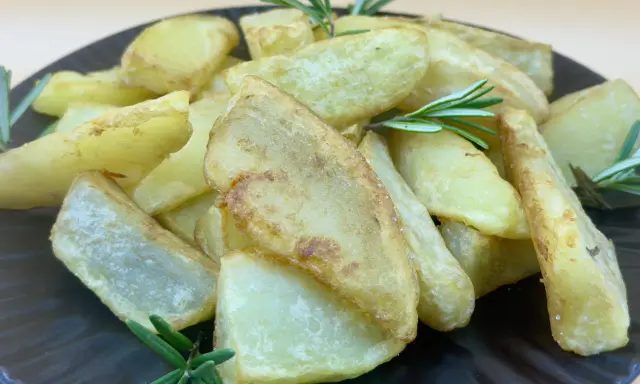 Patatas gajo doradas y crujientes, adornadas con ramitas de romero fresco, servidas en un plato oscuro.