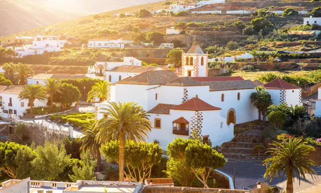 Villaggi turistici a Fuerteventura, con case bianche, palme e una chiesa con campanile, immersi nel sole dorato del tramonto.