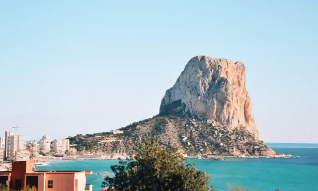 Widok na majestatyczną skałę Peñón de Ifach, symbol Costa Blanca atrakcje. Turkusowe morze i zabudowania miasta tworzą malowniczy krajobraz.