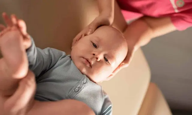 Delikatne dłonie osteopaty pediatrycznego obejmują główkę niemowlęcia, zapewniając mu komfort i wsparcie podczas terapii.